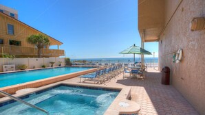 A pool area with a hot tub, lounge chairs, and a view of the ocean.