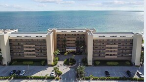 A multi-story hotel with a central courtyard, parking area, and a view of the ocean.