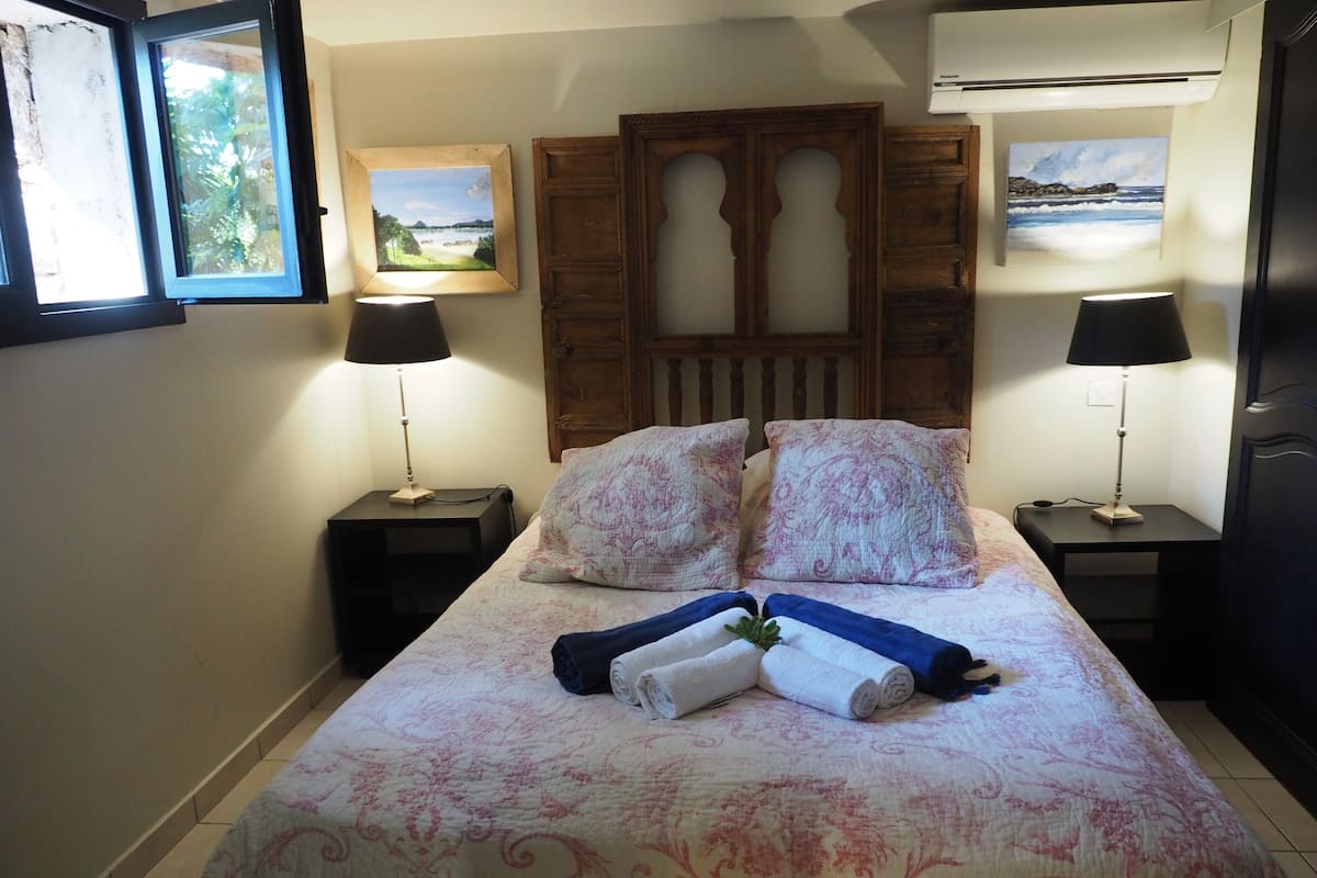 Cama bem arrumada com toalhas dobradas, dois mesas de cabeceira com abajures, cabeceira de madeira e duas fotos emolduradas nas paredes.