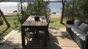 A wooden deck with a table and chairs, a wicker sofa, and a view of a lake with mountains in the background. - Maranatha Porto Vecchio (Porto-Vecchio)