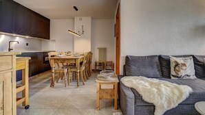 Eine moderne Küche mit Holzschränken, einem Esstisch und Stühlen. Ein graues Sofa mit Felldecke und Zierkissen.