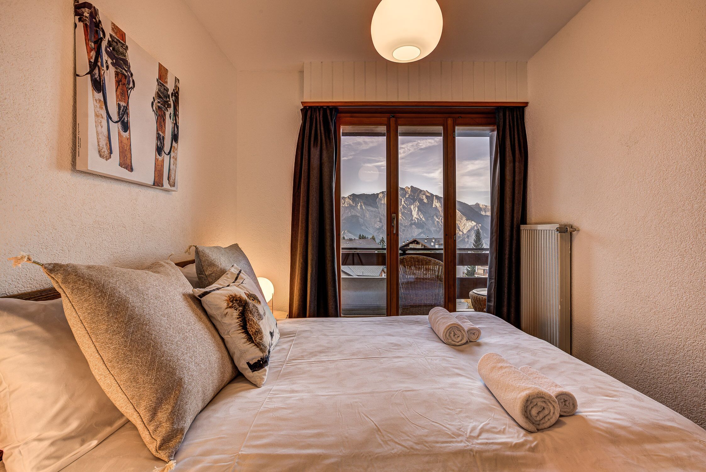 Une chambre d’hôtel avec un lit, des oreillers, une vue sur les montagnes par la fenêtre et un tableau au mur.