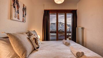 Une chambre d’hôtel avec un lit, des oreillers, une vue sur les montagnes par la fenêtre et un tableau au mur.