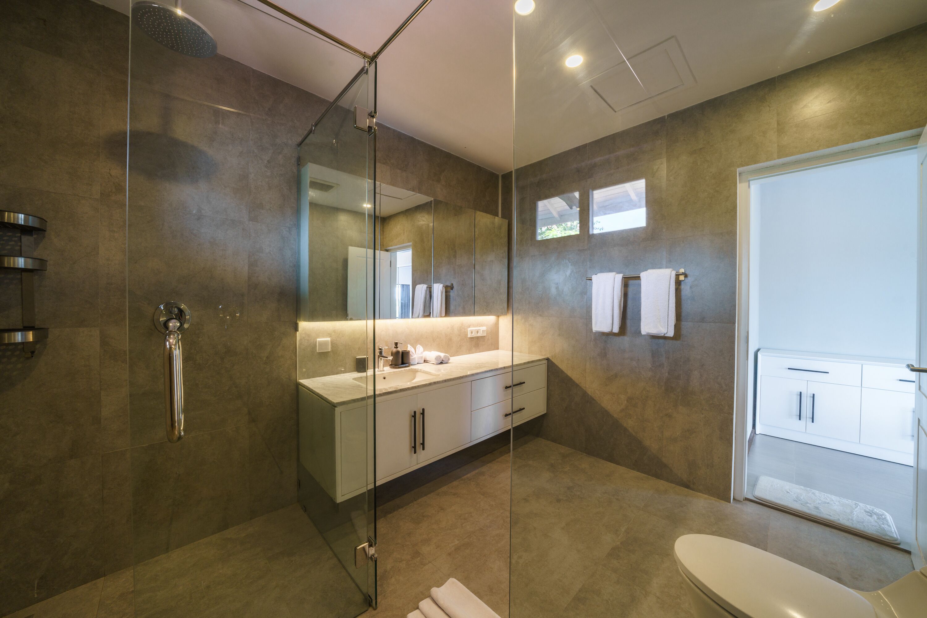 Un baño moderno con cabina de ducha de vidrio, un espejo grande y un tocador blanco con lavamanos.