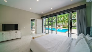 Un dormitorio moderno con una cama grande, televisión y vistas a una piscina.