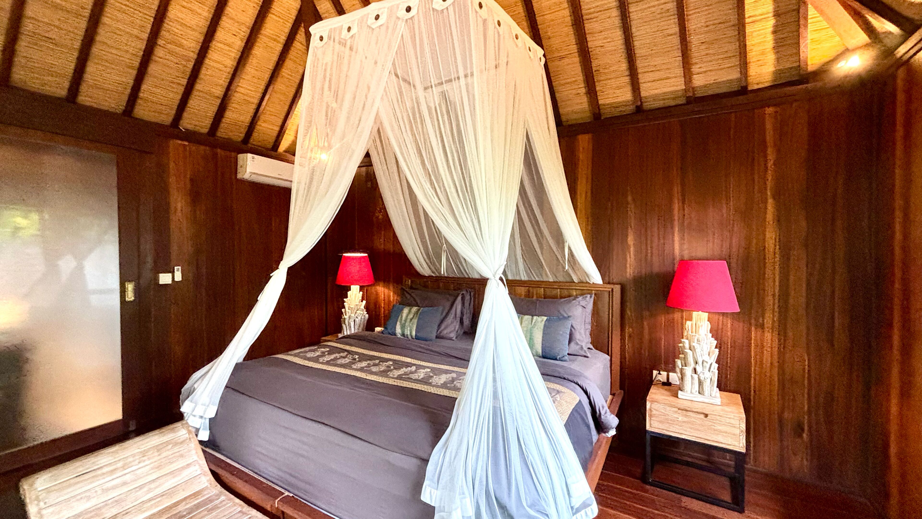 A four-poster bed with a canopy, two bedside tables with lamps, and wooden paneling on the walls.