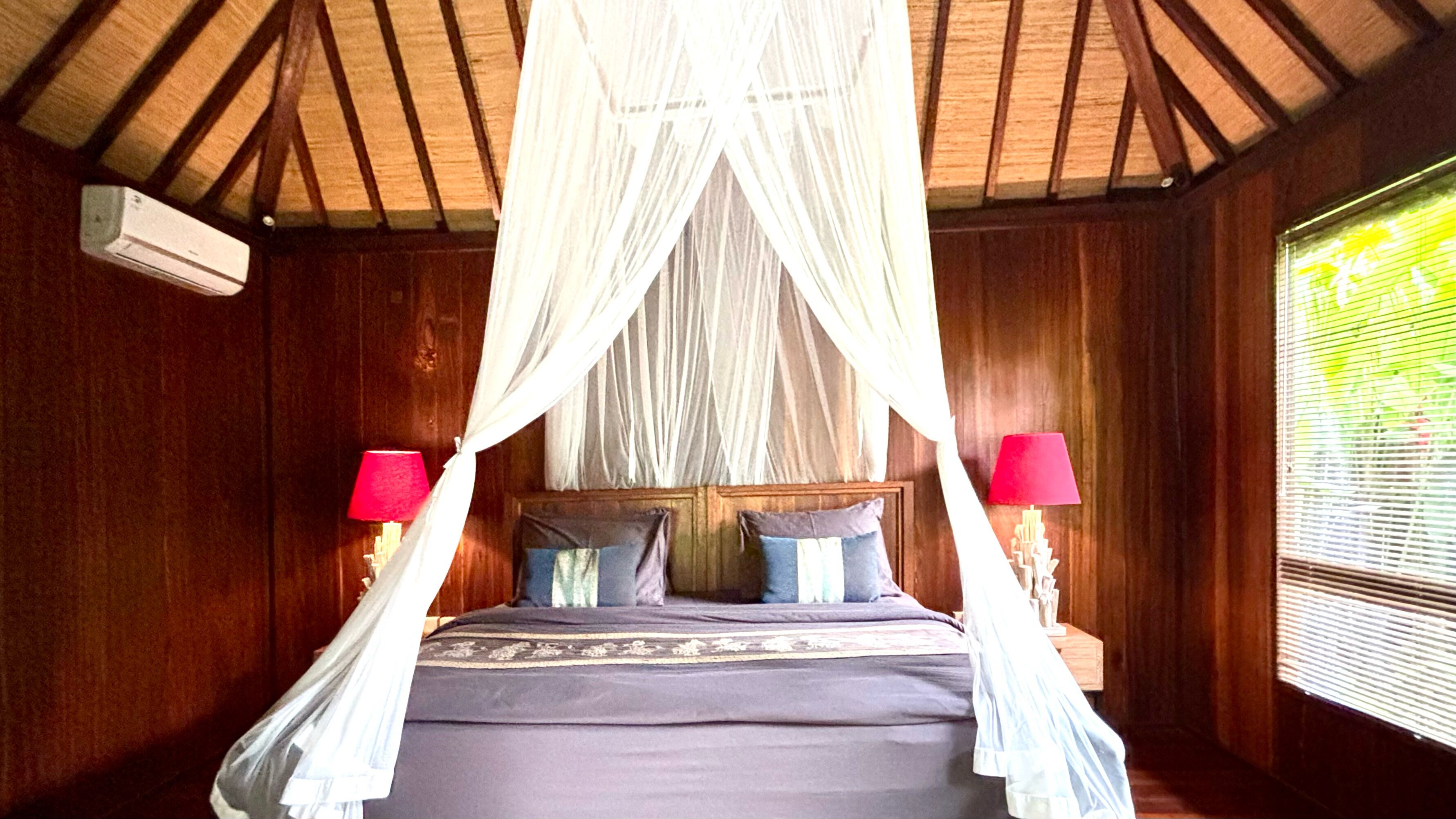 A bedroom with a canopy bed, wooden walls, and two bedside lamps.