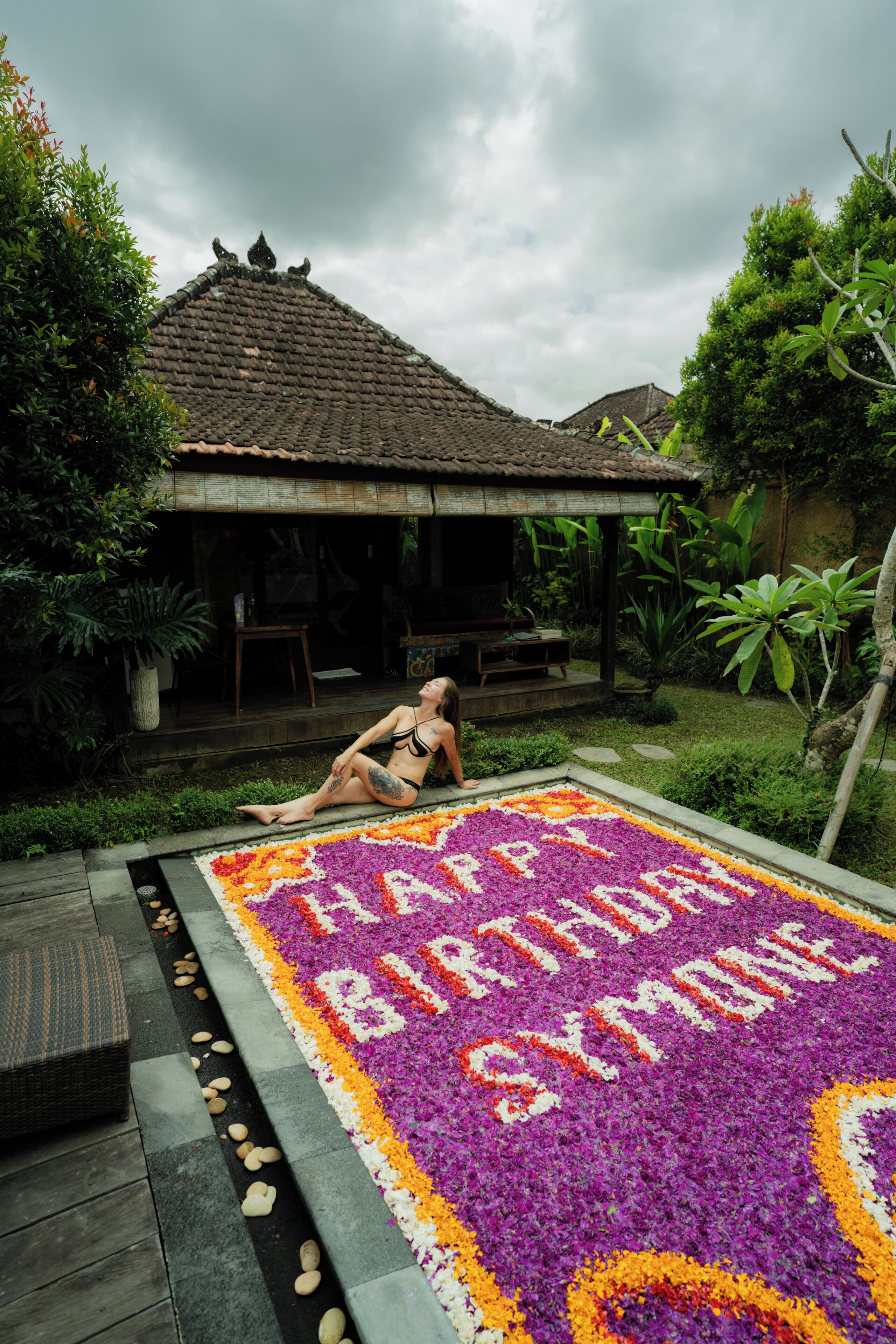 A woman sitting on a patterned floor with a house in the background.