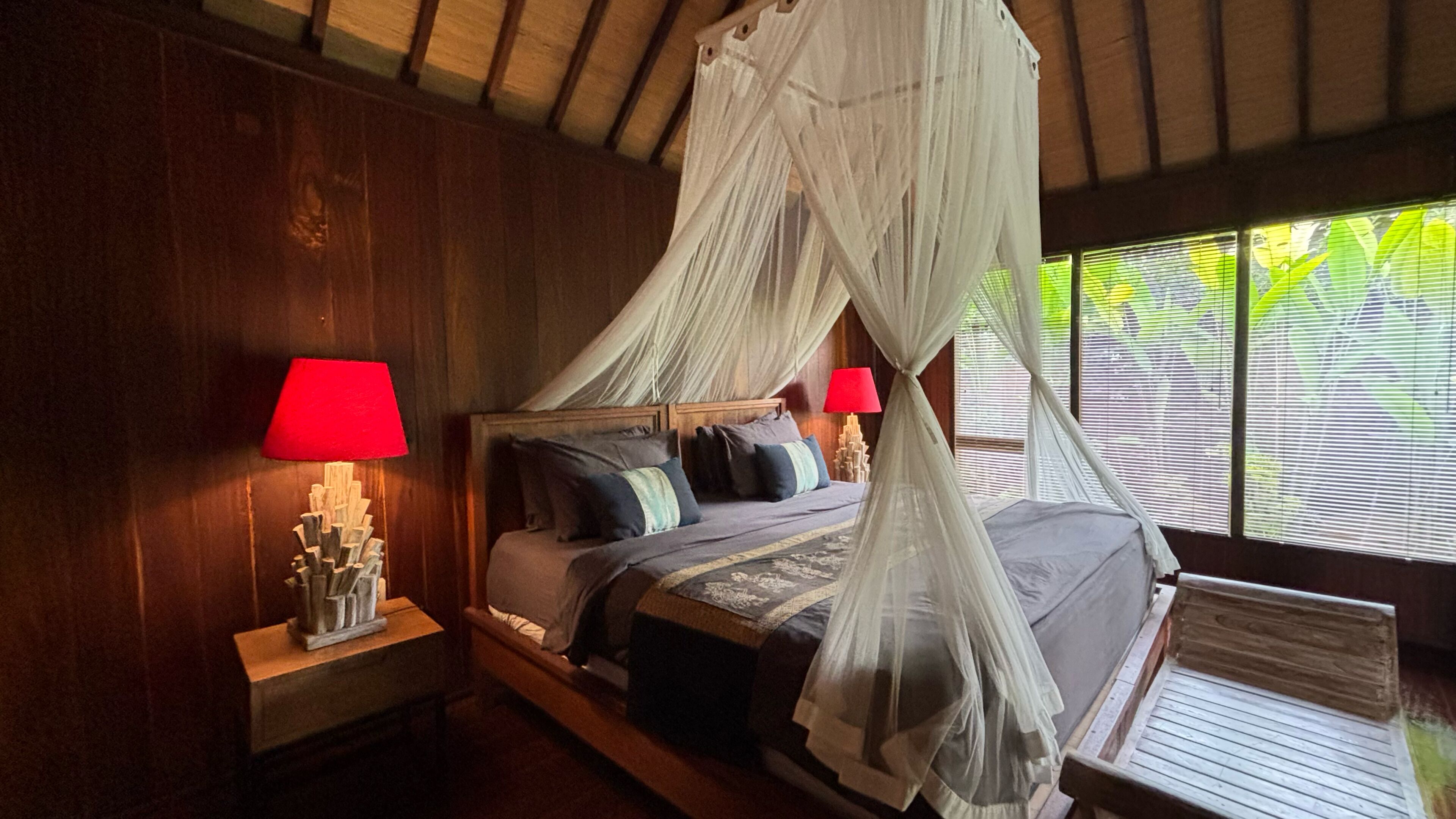 A bed with a canopy, wooden headboard, and bedside lamps.