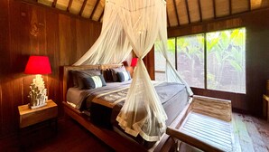 A wooden room with a bed, a nightstand, a red lamp, and a window with blinds. - NILUH Private Villas  (Ubud)
