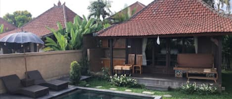 A poolside area with a tiled roof, lounge chairs, and a small seating area with a table and chairs.