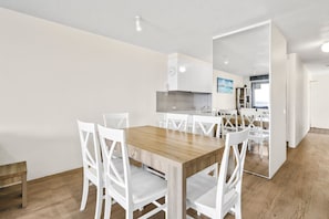 A modern kitchen with white cabinets, a wooden dining table, and white chairs. - Seaspray U6 Ocean Views & Direct Beach Access (Kings Beach)