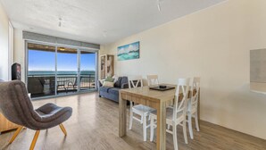 A spacious living area with a balcony overlooking the sea, a dining table with chairs, and a sofa. - Seaspray U6 Ocean Views & Direct Beach Access (Kings Beach)