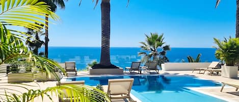 A pool area with lounge chairs and a view of the ocean.