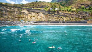 A coastal area with clear turquoise waters, people surfing, and a rocky hillside with vegetation. - CHARCO DEL VIENTO, vistas al mar con terraza y jar (Los Realejos)
