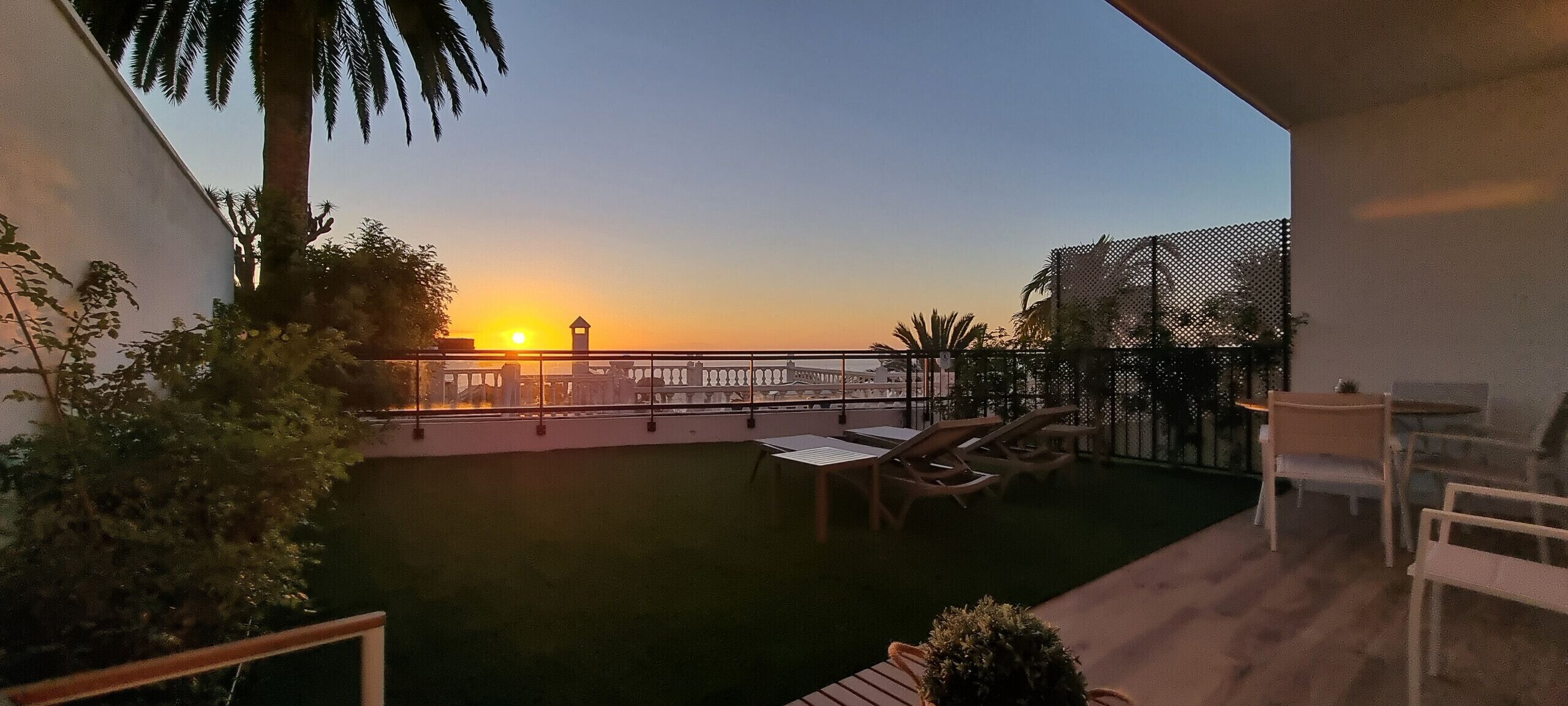 Un balcón con vista al atardecer, una piscina pequeña y mobiliario exterior.