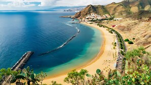 A coastal landscape with a beach, a rocky outcrop, and a settlement with colorful buildings.