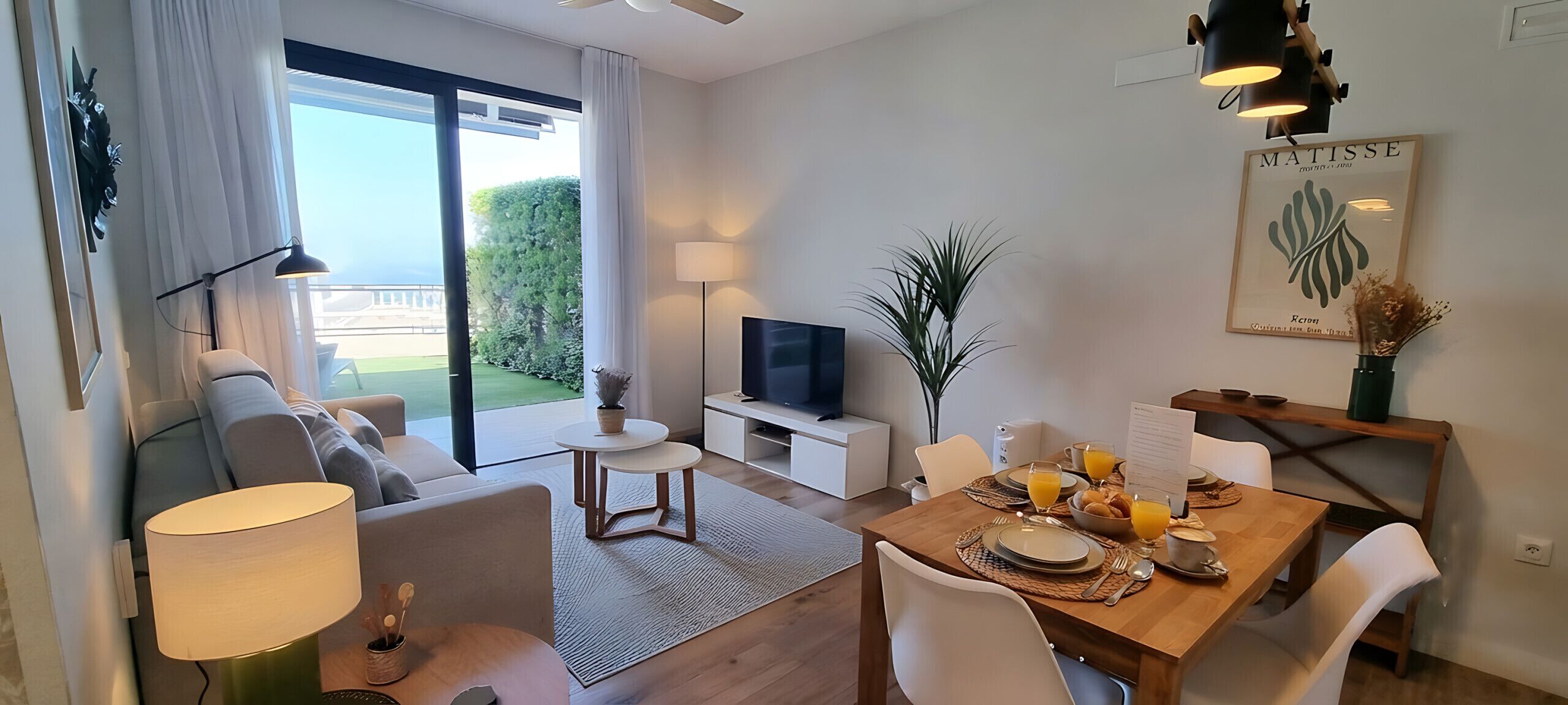 Ein modernes Wohnzimmer mit Sofa, Fernseher, Esstisch und Balkonblick.