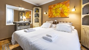 Une chambre d’hôtel avec un grand lit, une commode en bois, un miroir et un luminaire fixé au mur.