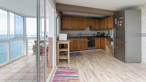 Ett modernt kök med träskåp, ett kylskåp i rostfritt stål och utsikt över havet genom stora fönster.