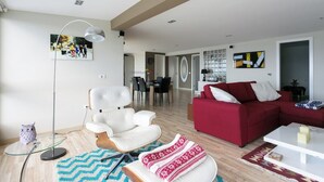 Ett modernt vardagsrum med en röd soffa, en vit fåtölj och ett soffbord i glas. Längre bak i rummet finns en matplats med ett bord och stolar.