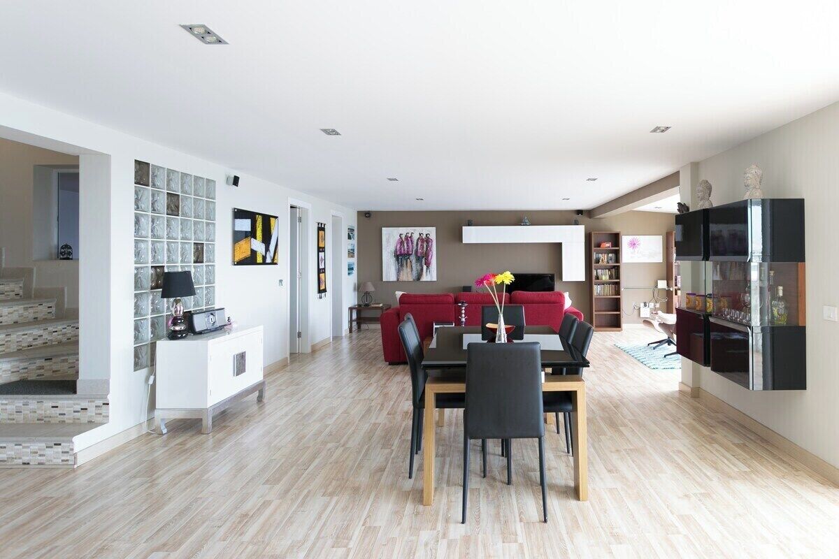 A spacious living area with a dining table, red sofa, and a kitchen area with a refrigerator and shelves.