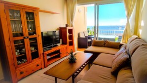 A living room with a television, wooden cabinet, sofa, and a view of the sea through a sliding glass door. - Coast, 4 people, sea and pool view, free WiFi  (Porís de Abona, Santa Cruz de Tenerife)