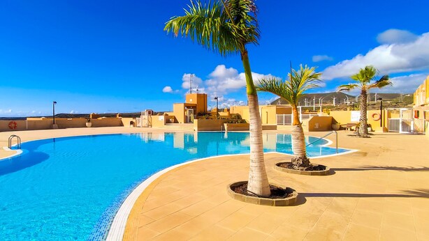 A swimming pool with a curved edge, surrounded by a tiled deck and palm trees. - Coast, 4 people, sea and pool view, free WiFi  (Porís de Abona, Santa Cruz de Tenerife)