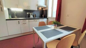 A compact kitchen with white cabinets, a black countertop, and a dining area with a table and chairs. - Charmant T2 34m2, 2e Étage au Coeur du Panier (Marseille)