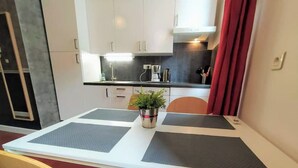 A dining area with a table set for two, a potted plant, and a kitchen in the background. - Charmant T2 34m2, 2e Étage au Coeur du Panier (Marseille)