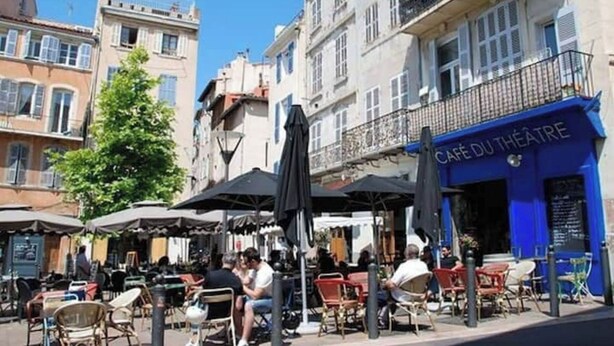 An outdoor café with tables and chairs, a blue building with 'CAFÉ DU THEATRE' signage, and a tree in the background. - Charmant T2 34m2, 2e Étage au Coeur du Panier (Marseille)