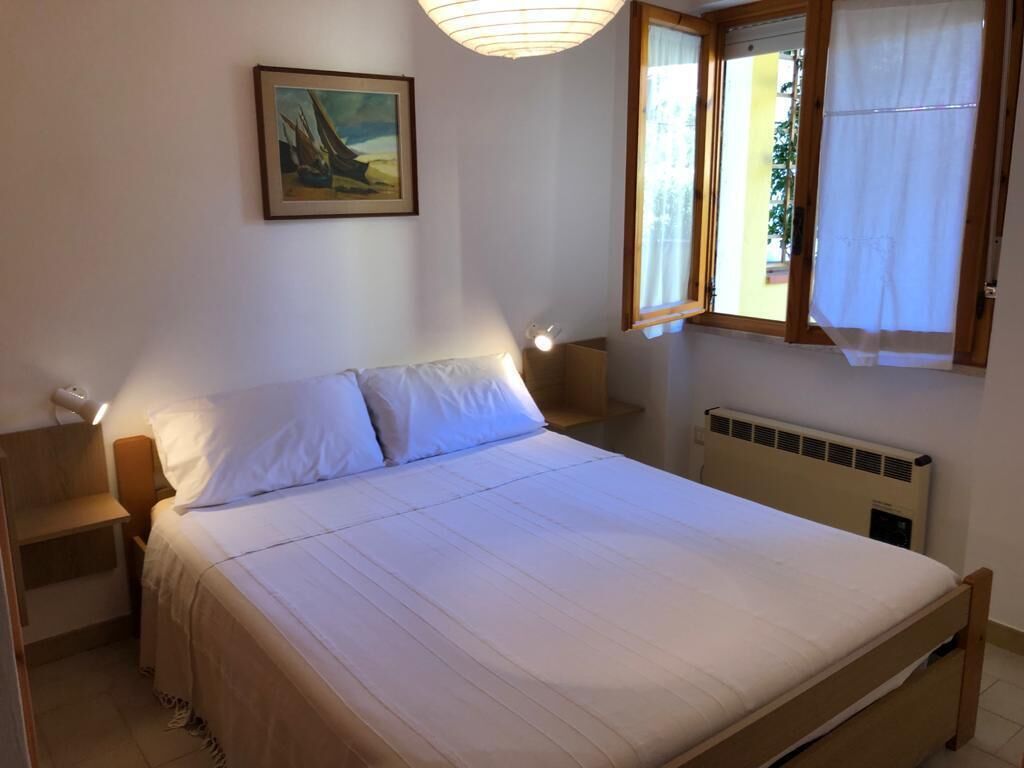 Un dormitorio con cama, mesitas de noche, una lámpara de pared y cortinas en la ventana.