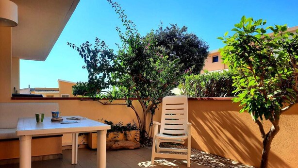 A patio with a table and a chair, surrounded by plants and a clear sky. - Baia Asinara - Appartamento Fronte Mare Castelsardo (Lu Bagnu)