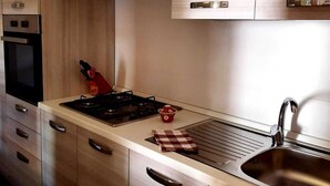 A modern kitchen with wooden cabinets, stainless steel appliances, and a built-in oven. - Baia Asinara - Appartamento Fronte Mare Castelsardo (Lu Bagnu)