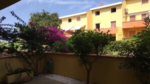 A courtyard with a yellow building, a small tree, and a planter with green plants. - Baia Asinara - Appartamento Fronte Mare Castelsardo (Lu Bagnu)