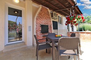 Eine Terrasse im Freien mit einer Ziegelwand, einem Tisch mit Stühlen und hängenden roten Blüten.