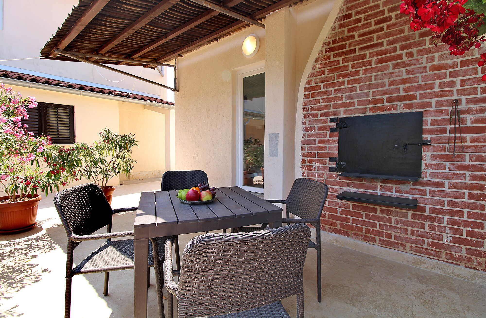 An outdoor patio with a brick wall, a table with chairs, a potted plant, and a television mounted on the wall.