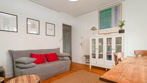 A living room with a grey sofa, red cushions, a wooden coffee table, a cabinet with glass doors, and a painting on the wall. - Appartement Hyper Centre (Brest)
