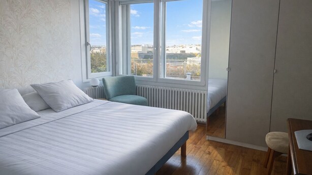 A bedroom with a large bed, a chair, a wardrobe, and a view of the city through large windows. - Appartement Hyper Centre (Brest)