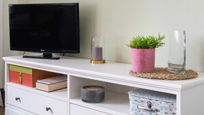 A white entertainment center with a flat-screen TV, a pink plant, and decorative items. - Appartement Hyper Centre (Brest)