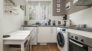 A compact kitchen with a washing machine, oven, and a window with a view of buildings. - Appartement Hyper Centre (Brest)