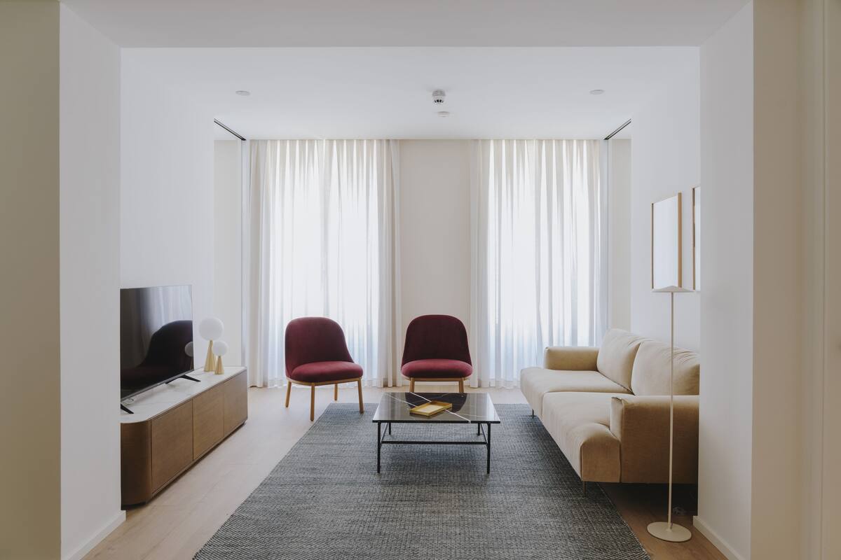 A modern living room with a flat-screen TV, two red armchairs, a beige sofa, a coffee table, and a floor lamp.