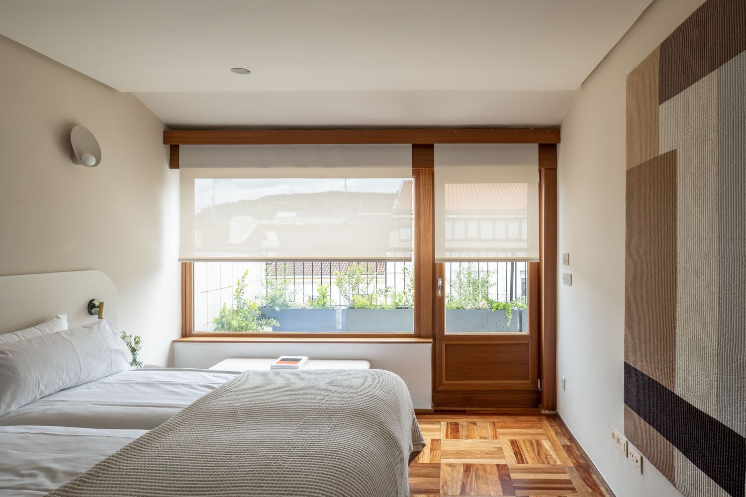 Une chambre avec une grande fenêtre, un lit, une table de chevet et une vue sur l’extérieur.