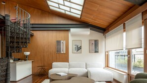 A modern living room with a wooden ceiling, a spiral staircase, a large window, and a sofa set. - The Passage Apartments (San Sebastián)