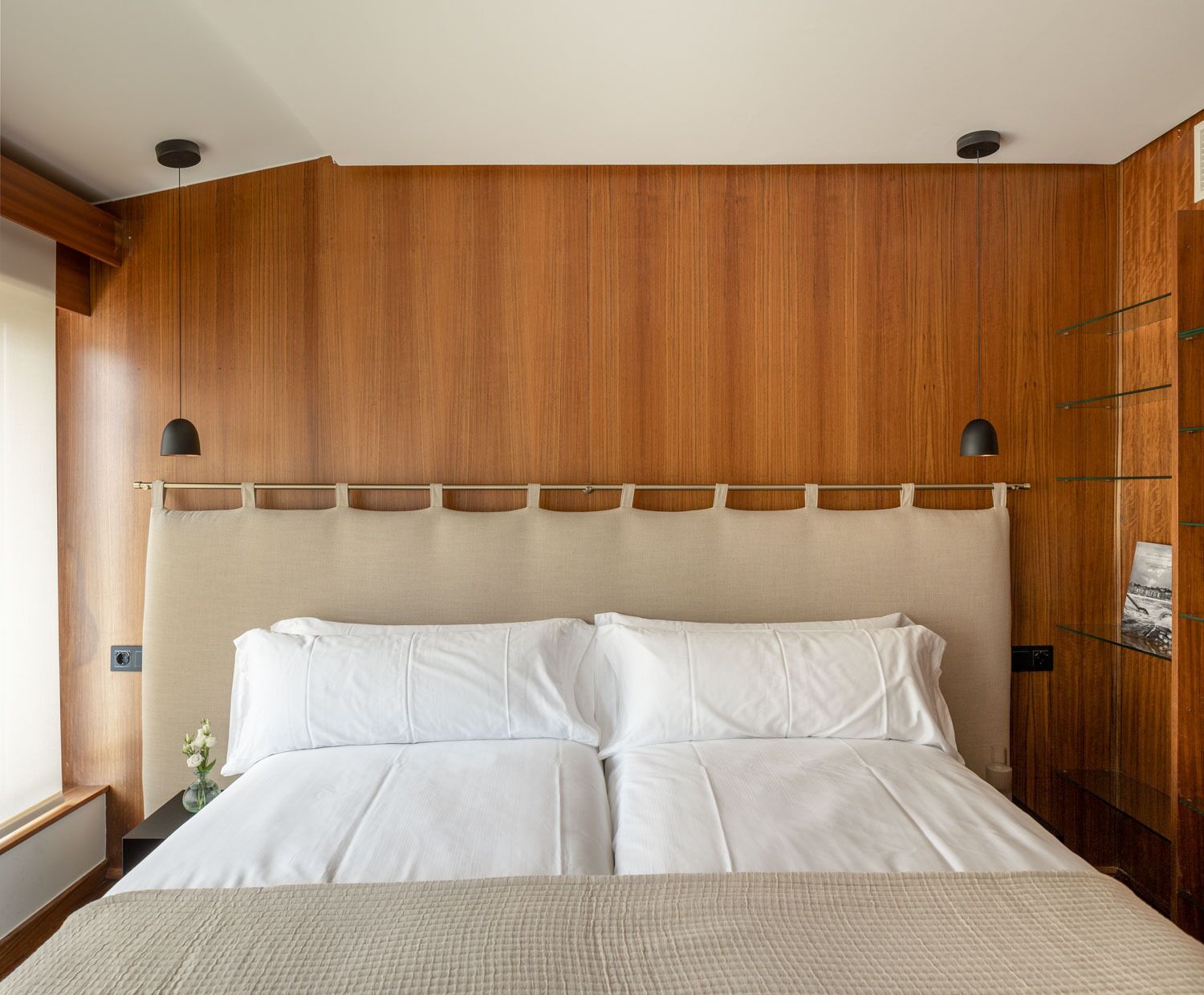 A hotel room with a wooden headboard, a bed with white linens, and a small nightstand with a vase of flowers.
