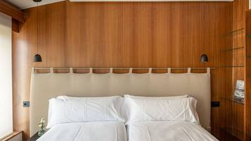 A hotel room with a wooden headboard, a bed with white linens, and a small nightstand with a vase of flowers.