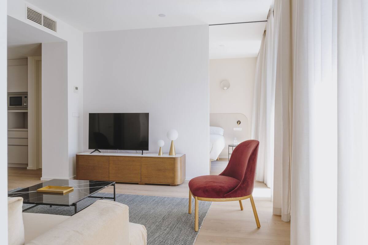 A modern living room with a flat-screen TV, a red chair, a wooden cabinet, and a sofa.
