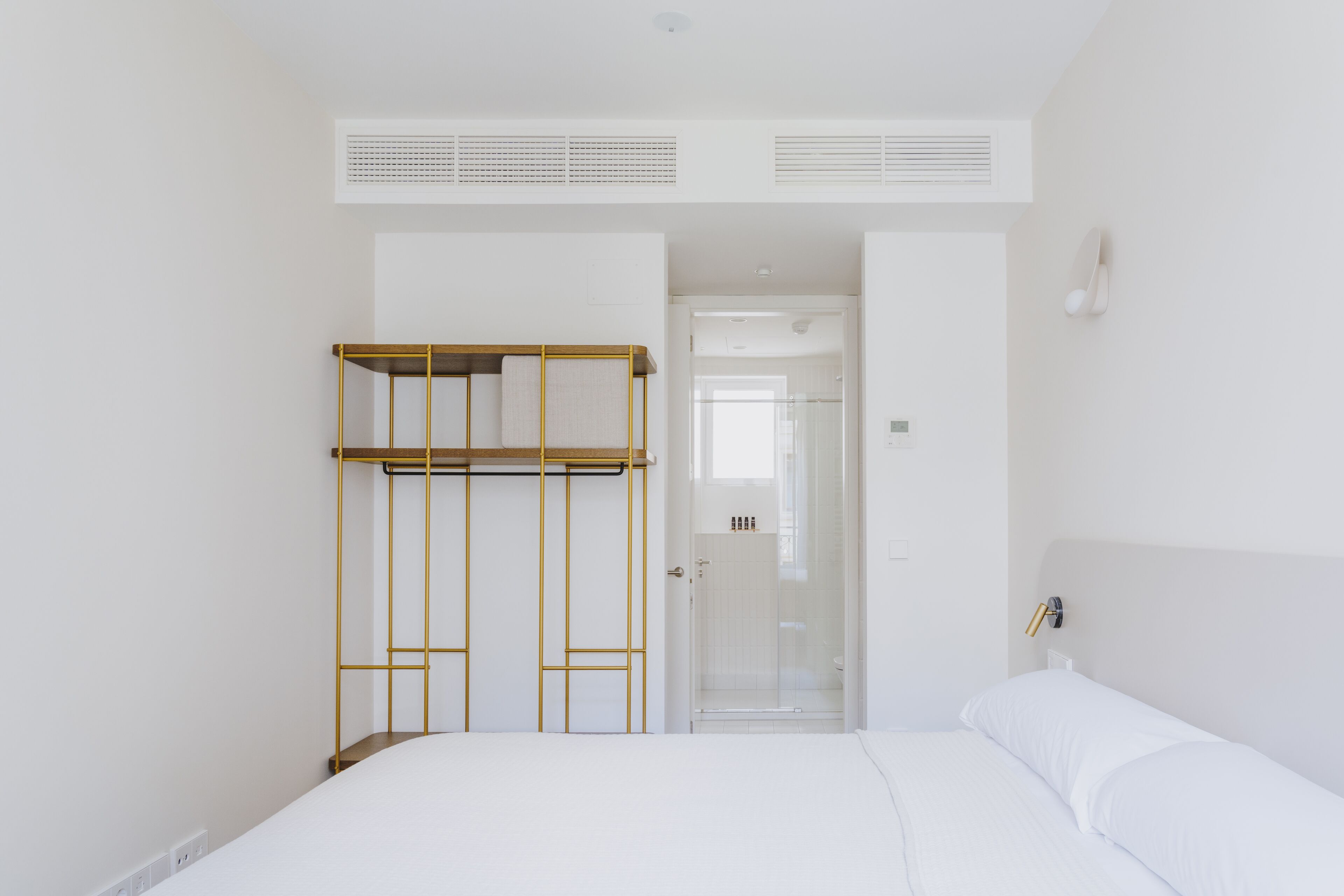 Ein schlicht eingerichtetes Hotelzimmer mit Stockbett, begehbarem Kleiderschrank und einem durch eine Glastür einsehbaren Badezimmer.
