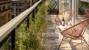 A balcony with wicker chairs, a table with a bottle and glass, and a view of buildings and a statue in the distance. - The Passage Apartments (San Sebastián)