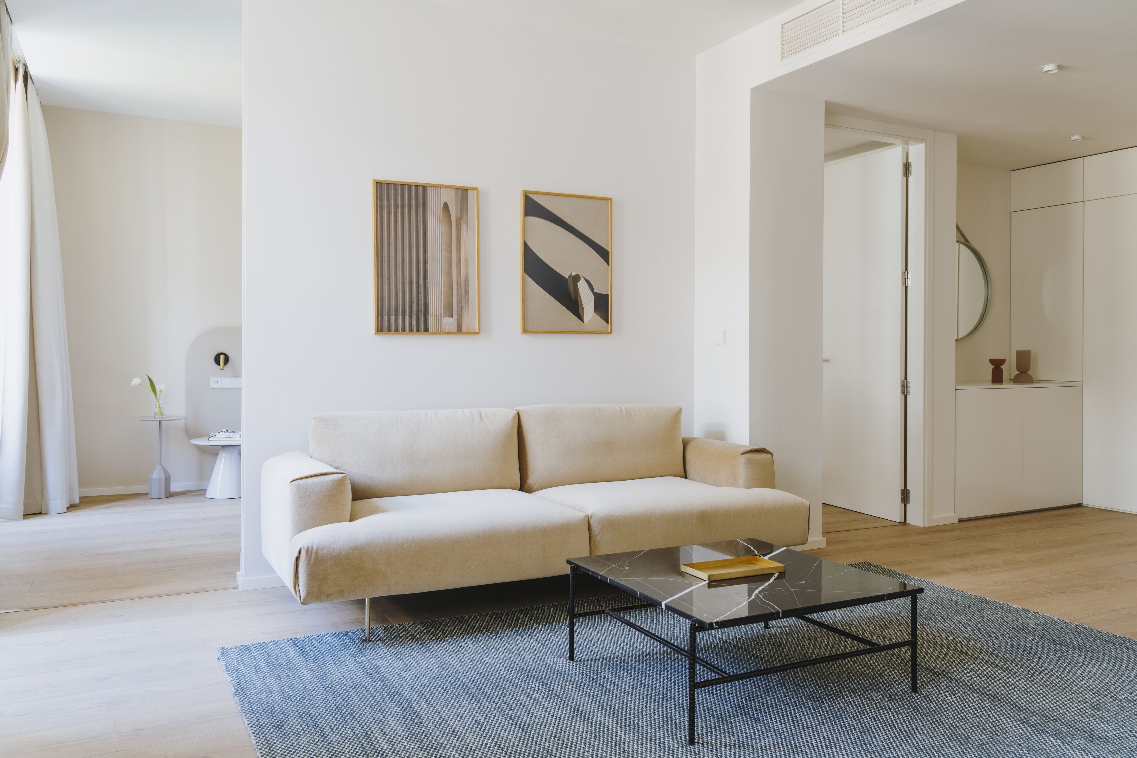 A modern living room with a beige sofa, a glass coffee table, and abstract wall art.